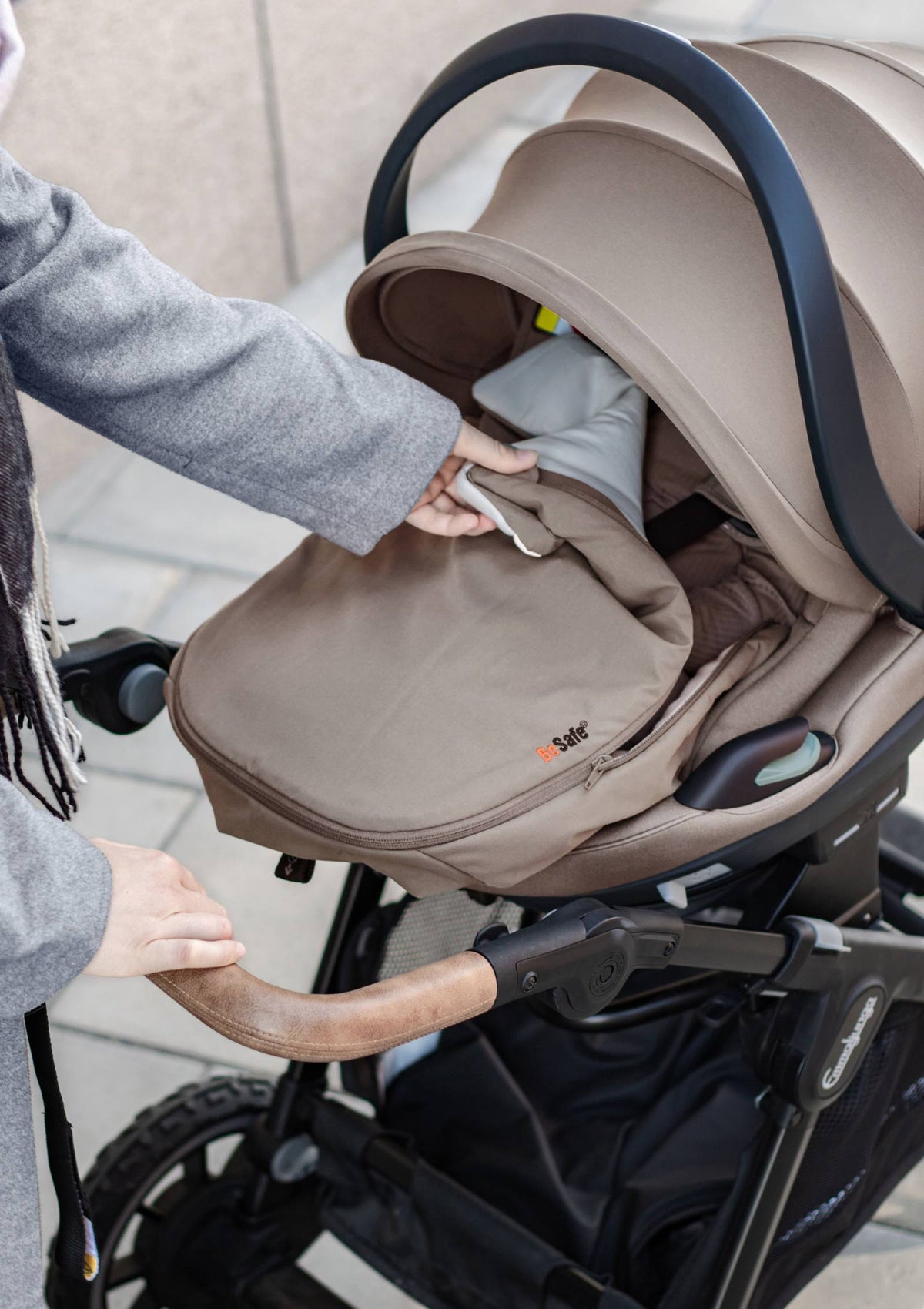 Frau öffnet BeSafe Wind & Weather Cover für Babyschale 'Go Beyond' Dark Sand
