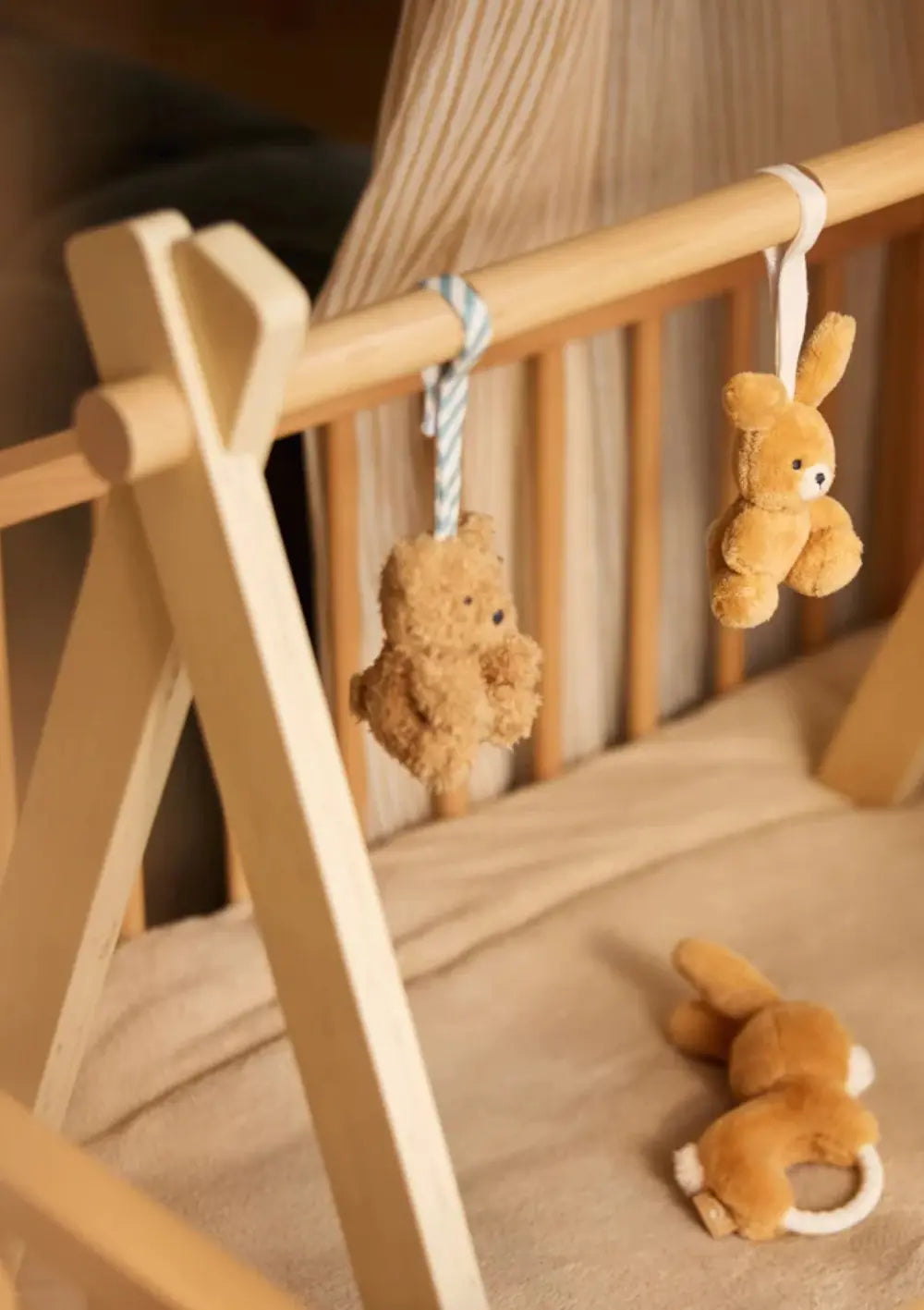 Das hölzerne Jollein Holz Spieltrapez Twist & Go steht über einer Babydecke, bespannt mit niedlichen Plüsch-Anhängern wie Bär und Hase.