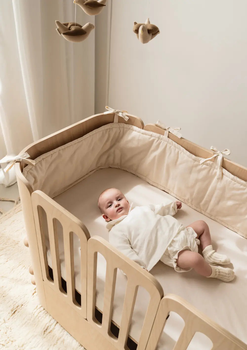Baby liegt in Nani Berlin 4-in-1 Babybett  – ausgestattet mit Nässeschutzauflage 'Nani Berlin x Sproutling'