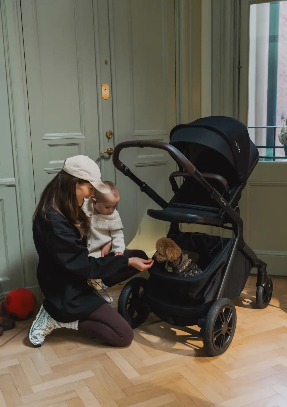 Frau und Baby streicheln Hund der im Korb des Nuna Sportwagens 'DEMI icon' Caviar sitzt