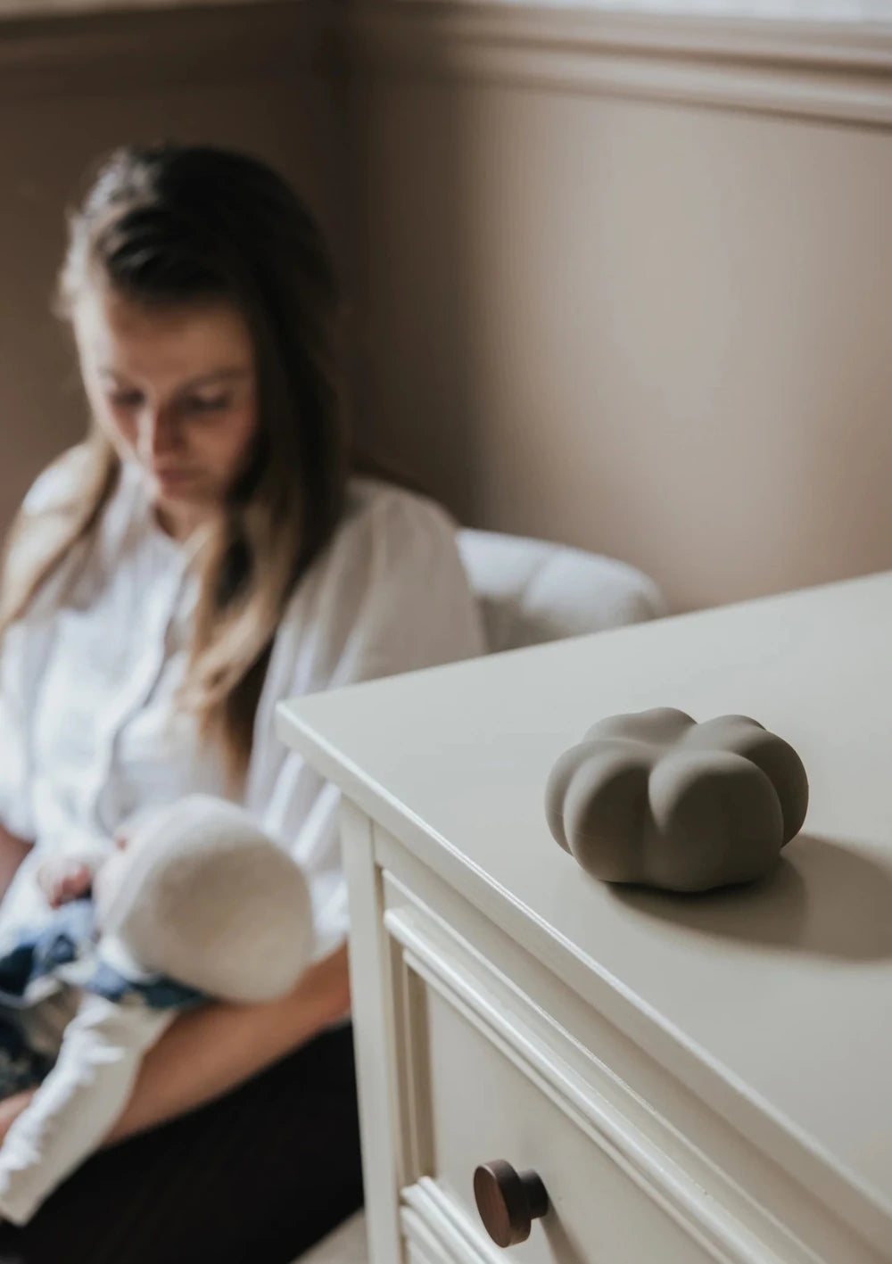 flow AMSTERDAM Nachtlicht Kleeblatt 'Luck' soft clay  leigt auf einer Kommode, dahinter sitzt eine Mutter mit Baby