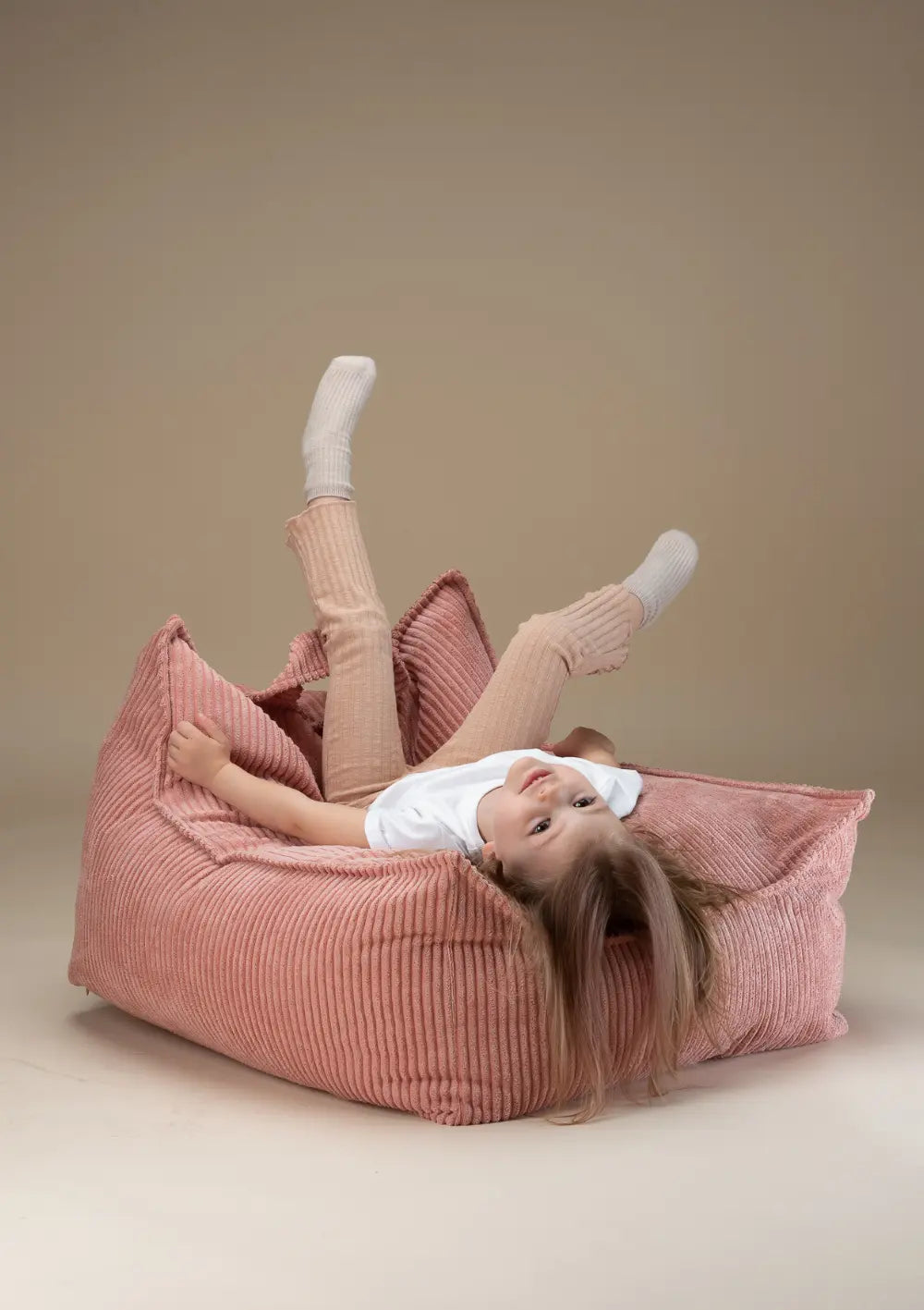 Ein Kind liegt kopfüber und fröhlich im rosafarbenen Wigiwama Sitzsack Cord Pink Mousse aus Breitcord und streckt die Beine in die Luft.