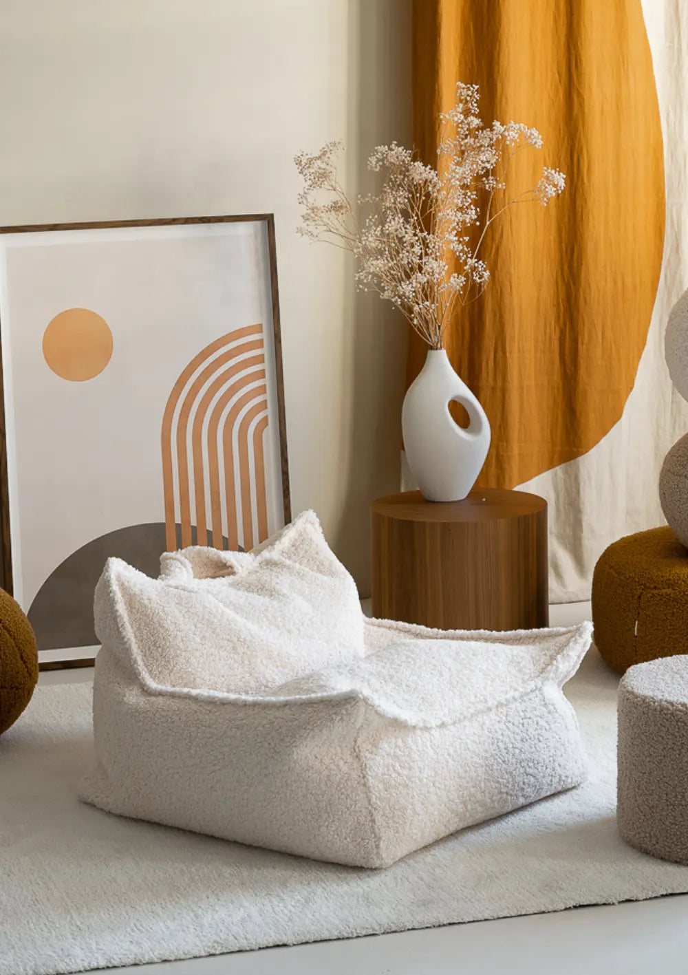 Der cremeweiße Wigiwama Sitzsack Teddy Cream White aus flauschigem Plüsch steht freistehend neben einem Holzbeistelltisch auf einem hellen Teppich.