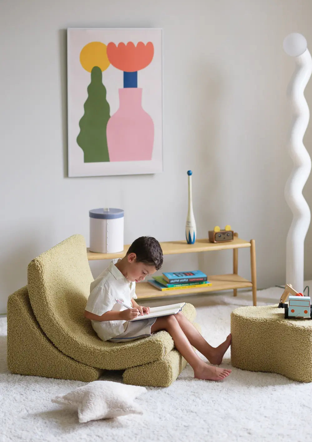 Ein Junge sitzt gemütlich im matcha-grünen Wigiwama Kindersessel Moon Chair Teddy Matcha aus kuschligem Teddy-Plüsch und malt in ein Buch.