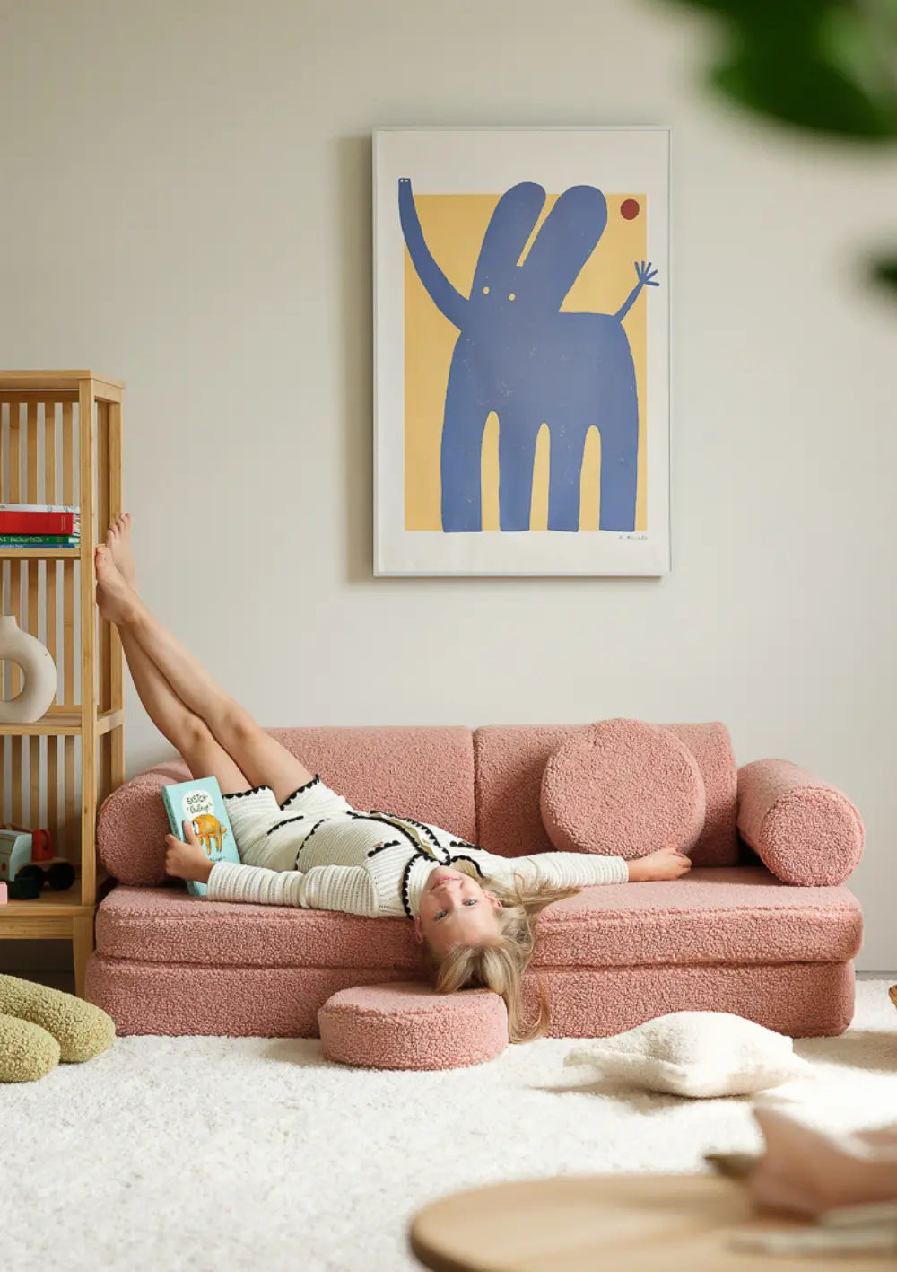 Ein Mädchen liegt rücklings entspannt auf dem rosafarbenen modularen Wigiwama Kindersofa Teddy Guava aus kuschligem Plüsch.