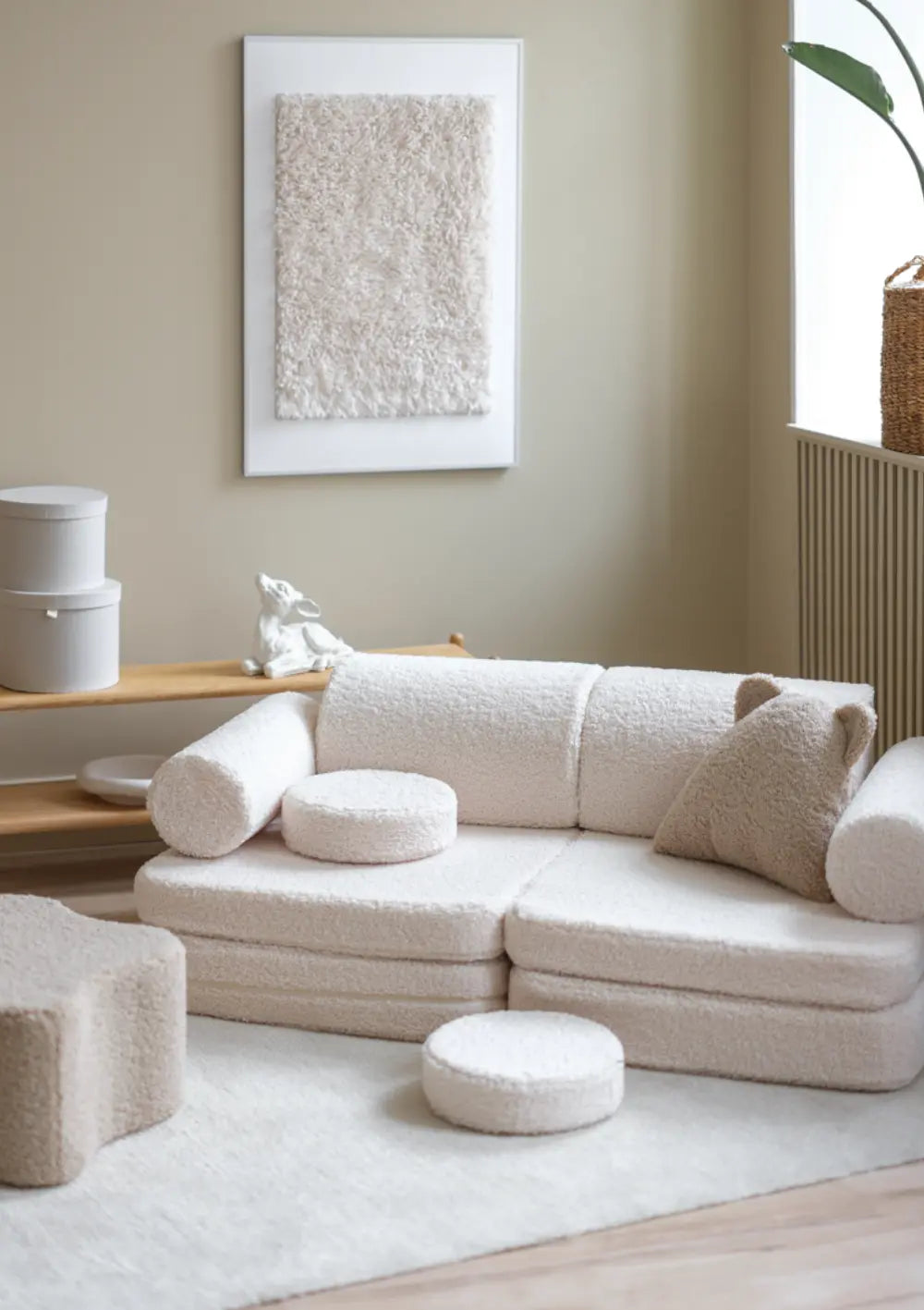 Das cremeweiße modulare Wigiwama Kindersofa Teddy Cream White aus kuschligem Plüsch steht mit Dekokissen in einem hellen Raum.