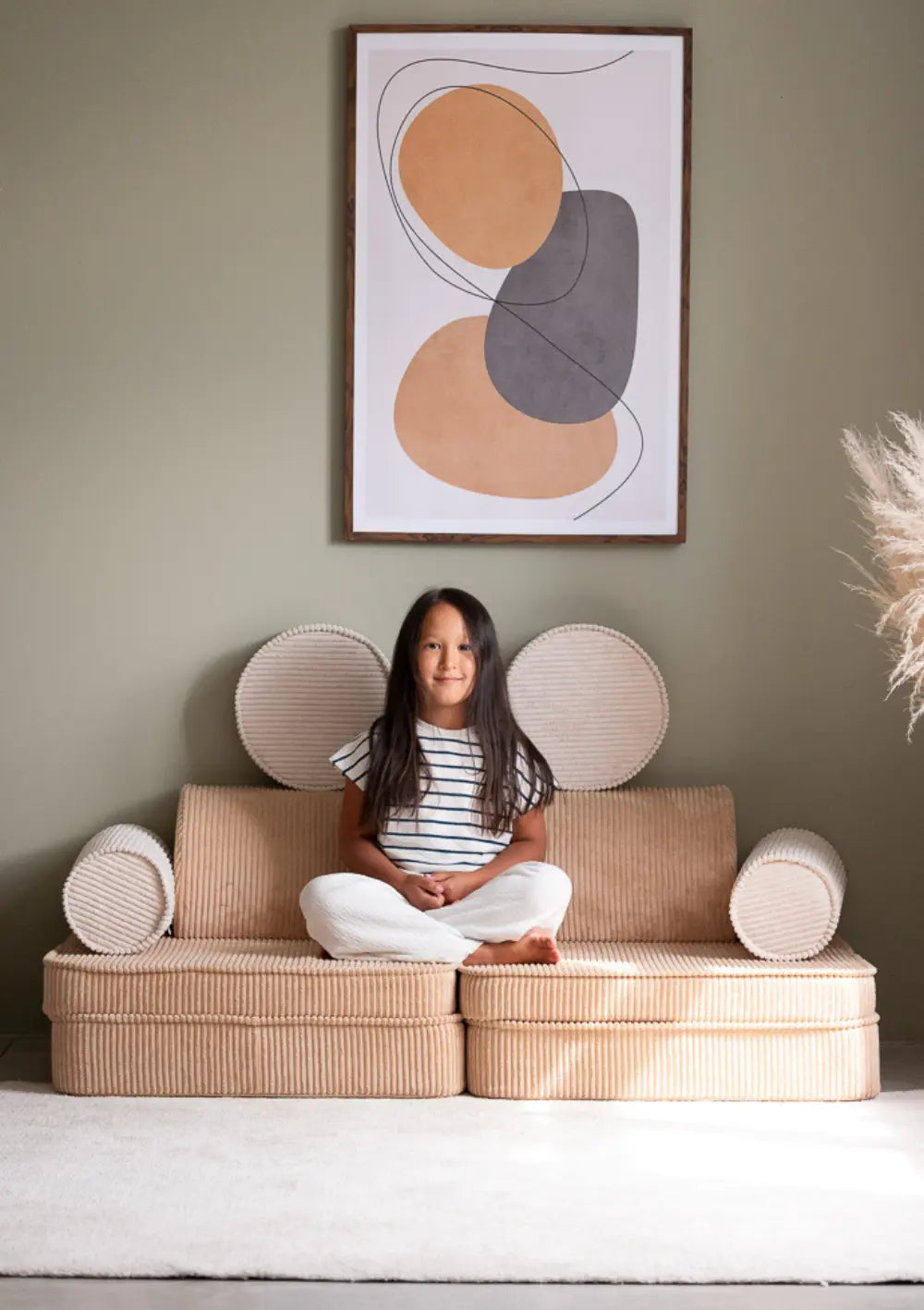 Ein Mädchen sitzt im Schneidersitz auf dem hellbraunen modularen Wigiwama Kindersofa Cord Brown Sugar aus Breitcord.